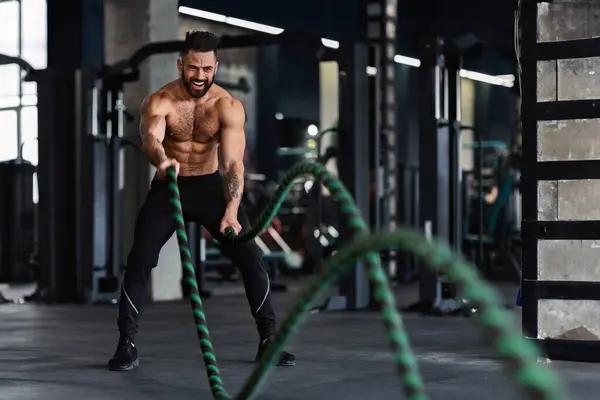 Stock image Crossfit training. Naked muscular man exercising with battle ropes at gym, free space