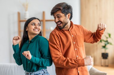 Genç Hintli bir çift, neşeli bir şekilde, aydınlık oturma odalarında dans eder, günlük giysiler giyer ve neşeli hareketlerle mutluluklarını ifade ederler.