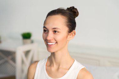 Parlak bir odada otururken topuzlu bir kadın kameraya gülümsüyor..