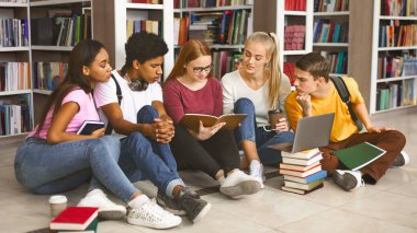 Kampüsteki kütüphanede yerde oturan ve eğitim alan, sınavlara hazırlanan, boş alan olan çeşitli öğrencilerden oluşan bir grup