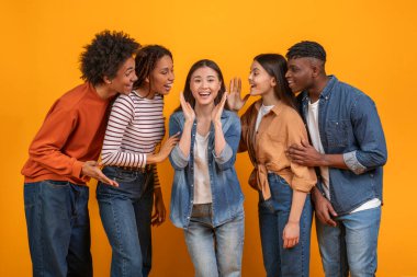 Çok ırklı arkadaşlar canlı sarı bir arka planın önünde dururlar. Hepsi gülümsüyor ve merkezdeki kadına bir sır fısıldıyor gibi görünüyorlar.