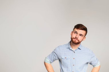 Düşünceli, genç, sakallı bir adam. Gri stüdyo arka planındaki fotokopi odasına bakıyor.