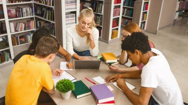 Çokuluslu öğrenciler daire içinde toplanıyor, kütüphanede birlikte ödev yapıyor, dizüstü bilgisayar kullanıyor