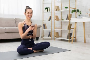 Evde egzersiz yapmak. Dinlenme, akıllı telefon kullanma ve müzik dinleme özelliğine sahip kadın