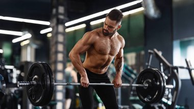 Modern bir spor salonunda sakallı bir adam halter kaldırıyor..