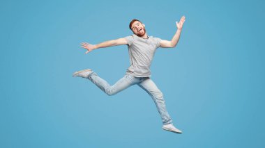 Komik Avrupalı adam havada zıplıyor ve mavi stüdyo arka planında dalga geçiyor, tam boy, boş alan