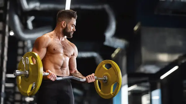 Stock image Handsome naked weightlifter lifting heavy barbell in gym, free space