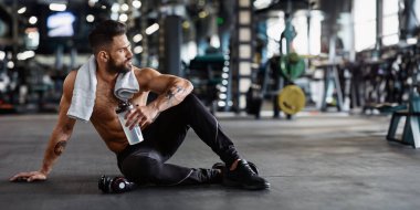 Spor kıyafetleri içinde kaslı bir adam spor salonunda oturur, idmandan sonra dinlenir, elinde su şişesi tutardı..