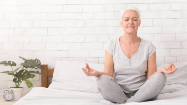 Meditasyon. Üst düzey kadın yatakta oturan lotus pozisyonu ve pratik anti-stres yoga, meditasyon boş alan