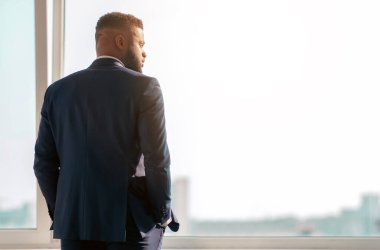 Takım elbiseli bir adam pencerenin yanında duruyor ve şehre bakıyor. Düşüncelere dalmış, geleceğini düşünüyor..