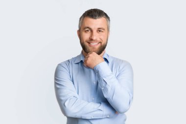 Mavi gömlekli bir adam fotoğraf için poz veriyor. Kameraya gülümserken rahat ve rahat bir tavır sergiliyor..