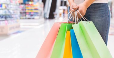 Bir kadın alışveriş merkezinde elinde rengarenk alışveriş torbalarıyla dikiliyor. Alış veriş yapıyor ve alışverişinden zevk alıyor gibi görünüyor, kesilmiş, kopyalama alanı