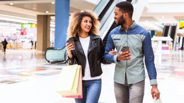 Mutlu bir Afro-Amerikan çifti alışveriş merkezinde yürüyor, neşeli bir sohbete dalıyorlar. Günlük kıyafetlerini giyip bir sürü alışveriş torbası taşıyorlar, paket kahve içiyorlar.