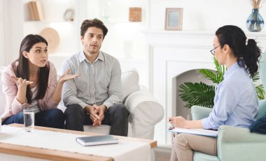 Duygusal bir erkek ve bir kadın bir kanepede oturmuş bir terapistle konuşuyorlar. Terapist dikkatle dinliyor ve profesyonel bir ortamda rehberlik öneriyor..