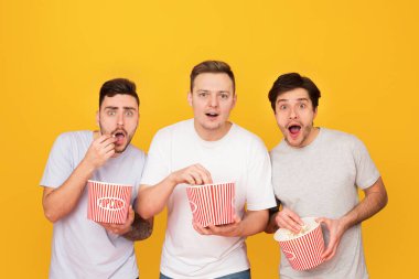 İlgilenen arkadaşlar patlamış mısır yeme ve turuncu arka plan üzerinde film izlerken