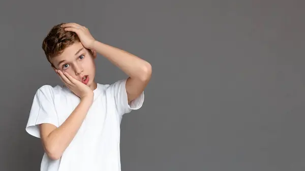 stock image A contemplative teenager with a hand on his head, isolated on a gray background, suggesting thoughtfulness in a youngster