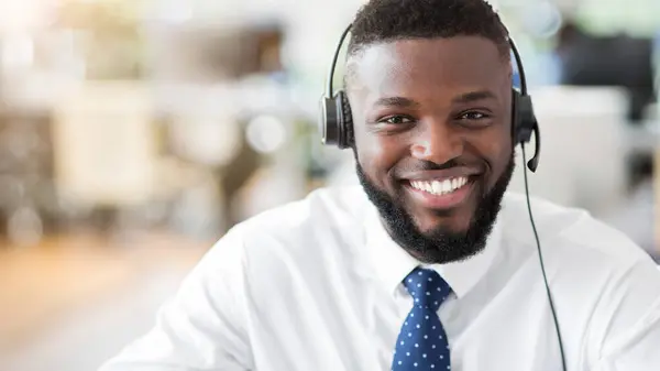 stock image A customer service representative wearing a headset smiles broadly while sitting at a desk in an office.