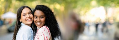 Arkadaşlık kavramı. Açık havada poz veren iki mutlu kız arkadaşın, kameraya sarılan ve gülümseyen çok ırklı kadınların, şehirde yürüyüş yapan neşeli dostların, yakın plan çekimleri, kopyalama alanının kopyaları.