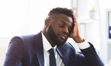 Yorgun, genç, Afro-Amerikan iş adamı. Dizüstü bilgisayarla çalışıyor. Alnına dokunuyor, uzayı kopyalıyor.