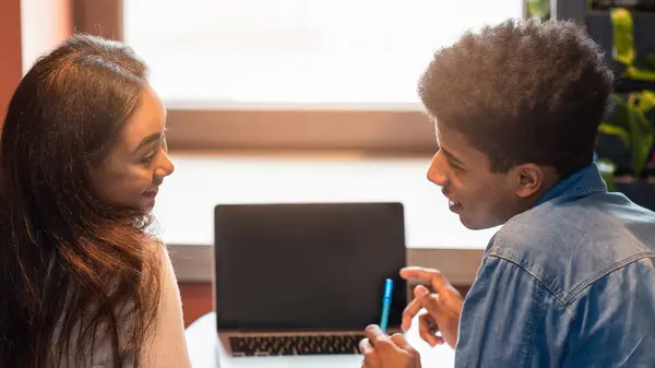 stock image Two black students are engaged in a discussion over a laptop in a bright, modern office setting. They seem focused and collaborative, working together on a project during the day.