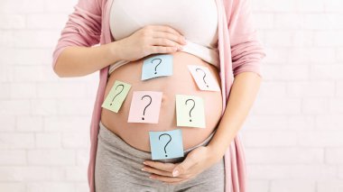 Karnında soru işaretleri olan hamile bir kadın. Düşünceli ve düşünceli görünüyor. Hamileliğin ve anneliğin belirsizlikleri üzerine kafa yoruyor gibi..
