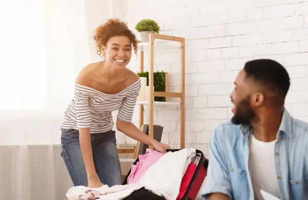 stock image African American couple in a room, unpacking clothes from suitcases. The man is folding shirts while the woman hangs dresses in the closet, back from trip