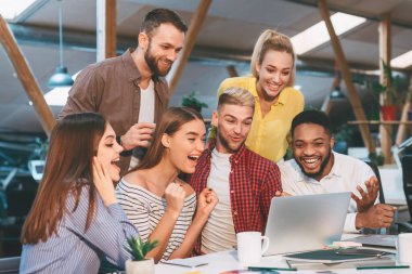 Şanslı şirket takımı. Tasarımcılar başarılı proje farkındalığını kutluyorlar, dizüstü bilgisayara bakıyorlar