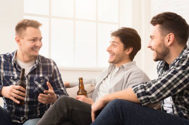 İyi ışıklandırılmış bir odada bira şişeleriyle sohbet eden üç genç adam.