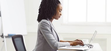 Odaklanmış bir Afro-Amerikan bayan ofis masasında bilgisayarı üzerinde çalışıyor. Sahne profesyonel ve organize, konsantrasyonu ve iş verimliliğini vurguluyor.