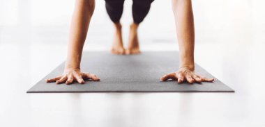 Kırpılmış bir kadın gri bir mindere yoga pozu verirken dengesini koruyor ve odaklanıyor. Çıplak ayakları ve elleri yüzeye bastırılmış. Bu da kuvvetini ve esnekliğini gösteriyor.