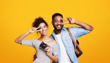Afro-Amerikalı erkek ve kadın turistler birlikte duruyor, sarı arka planda bir fotoğraf için çarpıcı pozlar veriyorlar. Turizm, seyahat kavramı