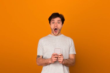 Avrupalı bir adam elinde akıllı bir telefonla abartılmış ve şaşırmış bir ifade sergiliyor.