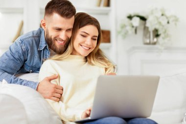 Bir adam ve bir kadın bir kanepede otururlar, önlerindeki dizüstü bilgisayara odaklanırlar..