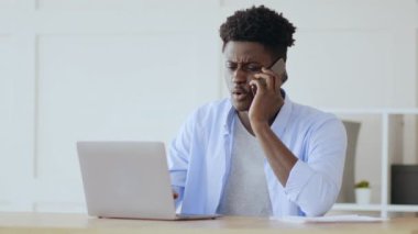 Uzak iş sorunları. Kızgın Afrikalı adam çalışanlarla telefonda tartışıyor, ev ofisinde çalışıyor.