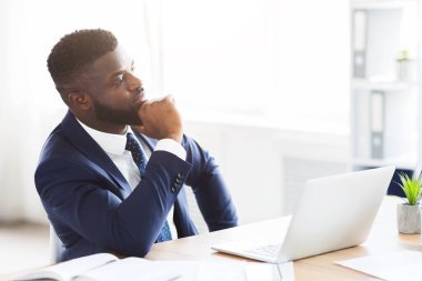 Düşünceli afro işadamı iş yerinde iş çözümleri üretiyor, çeneye dokunuyor ve boş alana bakıyor.