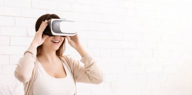 Genç bir kadın sanal gerçeklik kulaklığı kullanıyor ve parlak bir odada gülümsüyor. Dijital deneyimin tadını çıkarıyor gibi görünüyor..