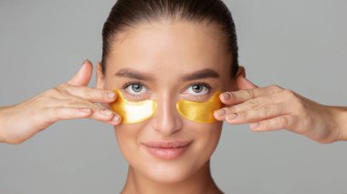 Gözlerinin üstüne altın maskeler takmış bir kadın güzellik gösterisi sergiliyor. Yamalar parlak ve yansıtıcıdır. Cildine çok yakındır..