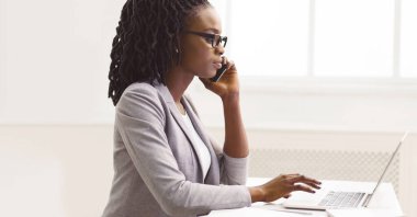 Yoğunlaşmış siyahi kadın CEO modern ofis içinde çoklu görev yapıyor, telefondaki verileri kontrol ediyor, kopyalama alanı, yan görünüm