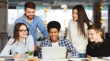 Bir grup insan kapalı bir masa etrafında toplandı. Aktif olarak bir dizüstü bilgisayara odaklanmış durumdalar, muhtemelen işle ilgili konuları tartışıyorlar veya bir projede işbirliği yapıyorlar..