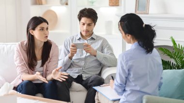 Kadın eşi duygularını paylaşırken, ilgisiz genç koca aile seansı sırasında terapistle telefon kullanıyor.