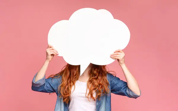 stock image A woman stands with outstretched arms, holding a large white cloud over hear face, expressing her opinion on pink background