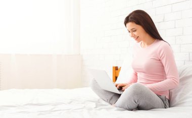 Yatakta oturan bir kadın dizüstü bilgisayar ekranına odaklanıyor. İşiyle ya da boş zamanlarında, elleri klavyeye basıyor, boşluğu kopyalıyor.