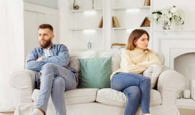 Bir adam ve bir kadın yan yana oturma odasında bir kanepede oturuyorlar..