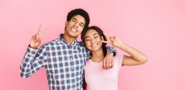 Mutlu çift pembe arka planda barış jesti yapıyor.