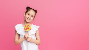 Tatlı yaz zamanı. Mutlu küçük kız şeker zevk, büyük renkli lolipop, pembe stüdyo arka plan ile gülümseyen