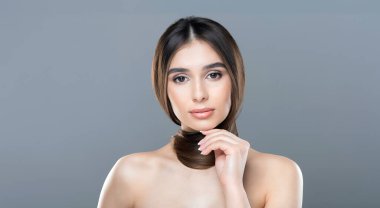 Uzun saçlı bir kadın poz veriyor, fotoğraf çektirmeye hazır. O, yüzünde hafif bir gülümseme ile kendinden emin ve rahat görünüyor. Geçmişi basit, dikkatin onun üzerinde olmasını sağlıyor..