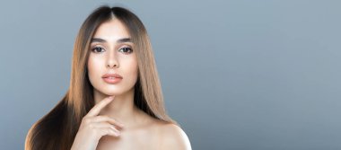 Uzun, düz saçlı bir kadın sakin bir ifadeyle doğrudan kameraya bakıyor. Eli nazikçe çenesinin yanında duruyor, ve düz gri bir arkaplanda duruyor, boşluğu kopyala