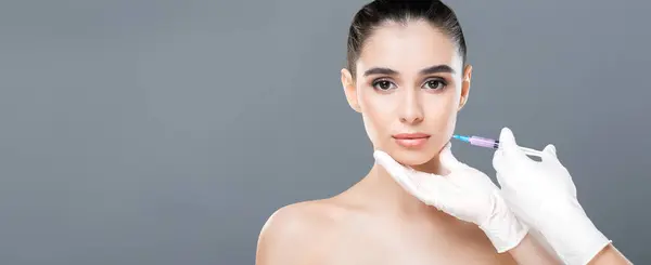 stock image A woman with a serious expression is receiving a cosmetic injection in a clinic. A medical professional with gloves carefully administers the treatment, copy space