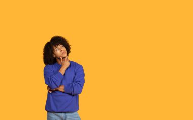 Kısa, kıvırcık kahverengi saçlı, mavi bir kazak ve kot pantolon giyen, yukarı ve sağa bakan, boşluğu kopyalayan genç adam.