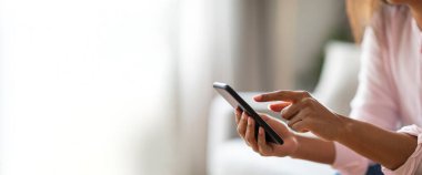 Oturma odasında oturan ve akıllı telefonuyla kayan bir kadın. Kadın sıradan giyinmiş, pembe bir gömlek, fotokopi odası.